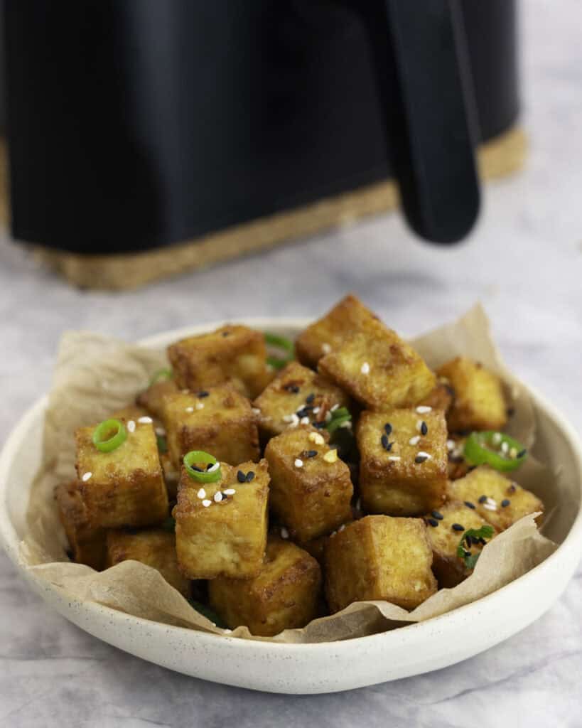 A small plate with crispy cubes of golden brown tofu garnished with sesame seeds and spring onion.