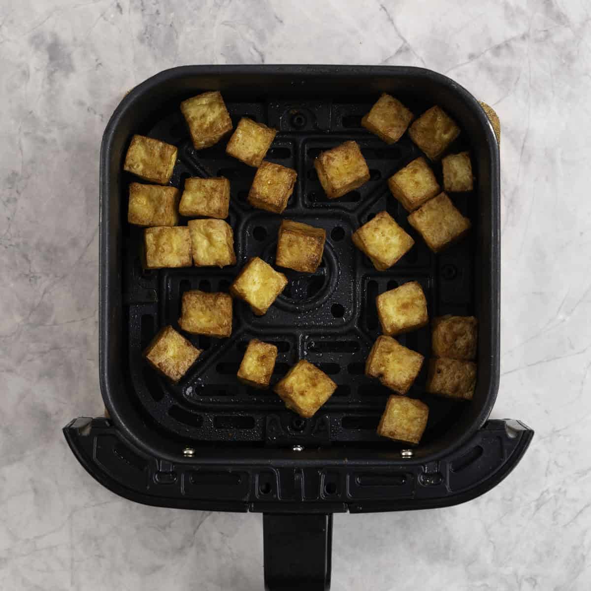 Cooked crispy tofu pieces cut into small cubes in the tray of an air fryer.