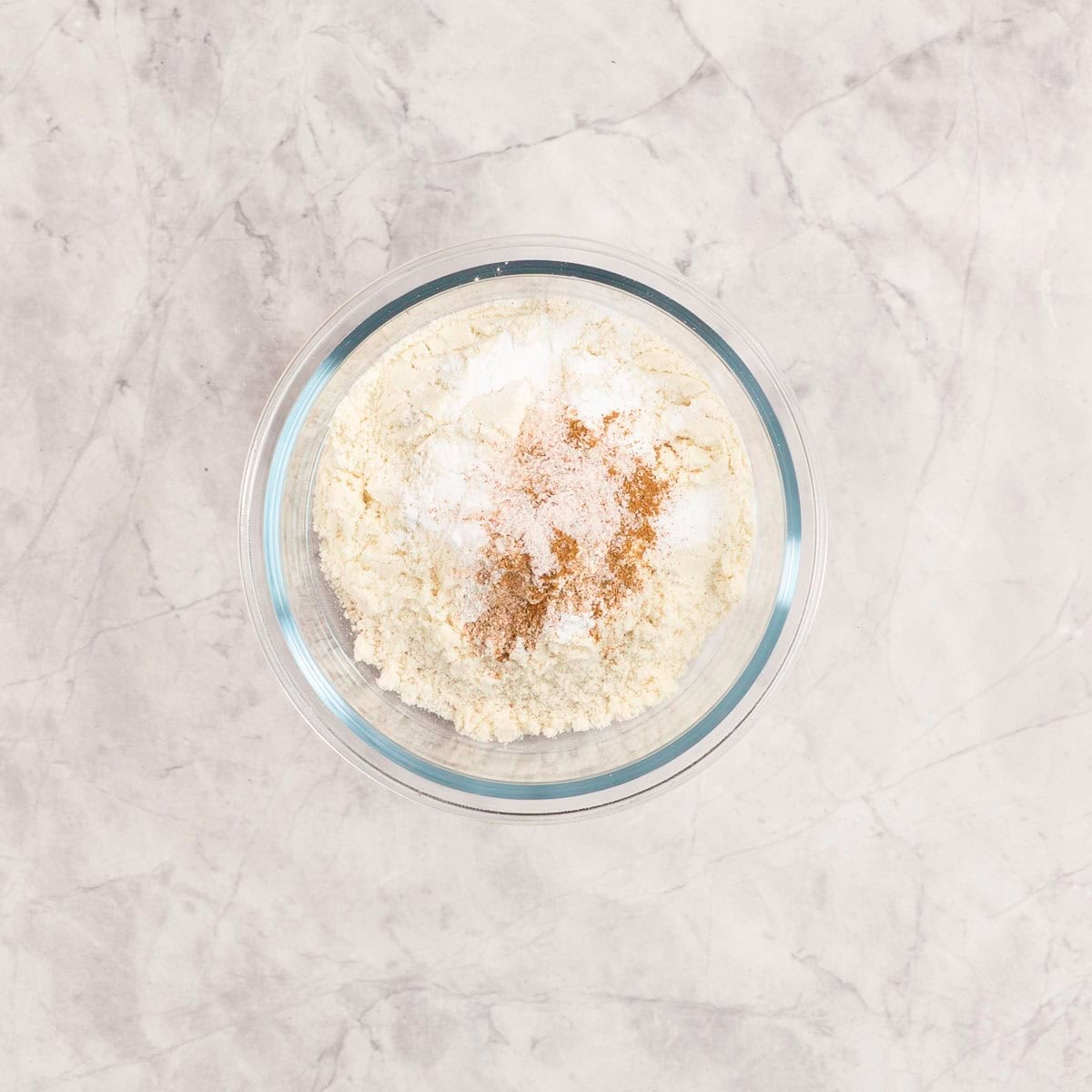 Dry ingredients in a small single serve glass bowl on marble bench top.