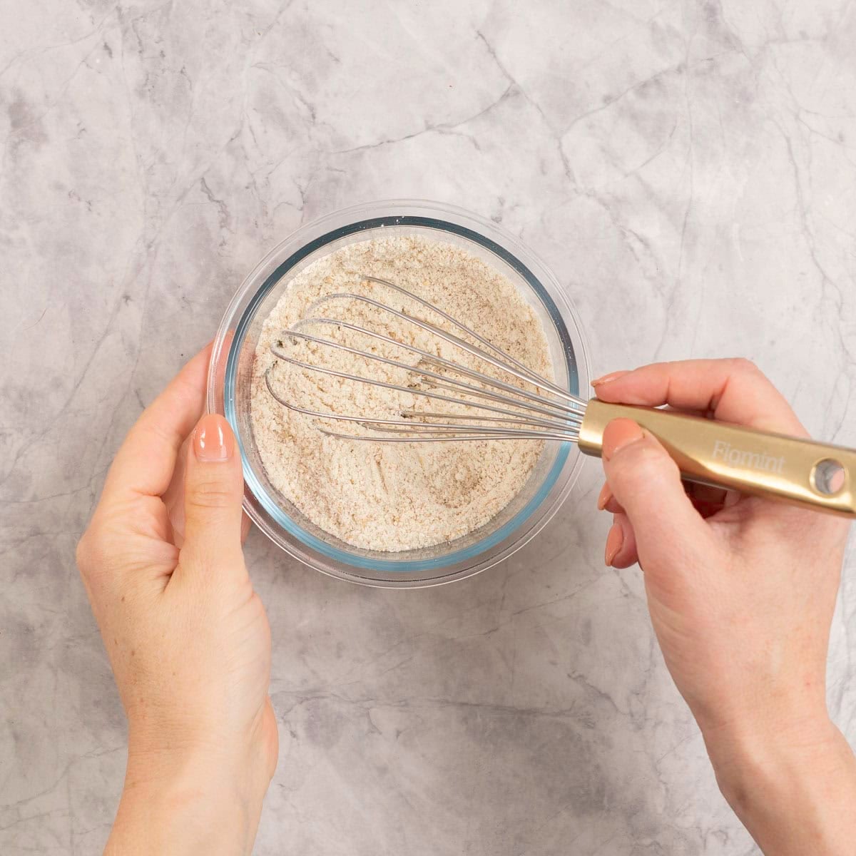 Woman's hand whisking dry ingredients in a small glass ramekin.