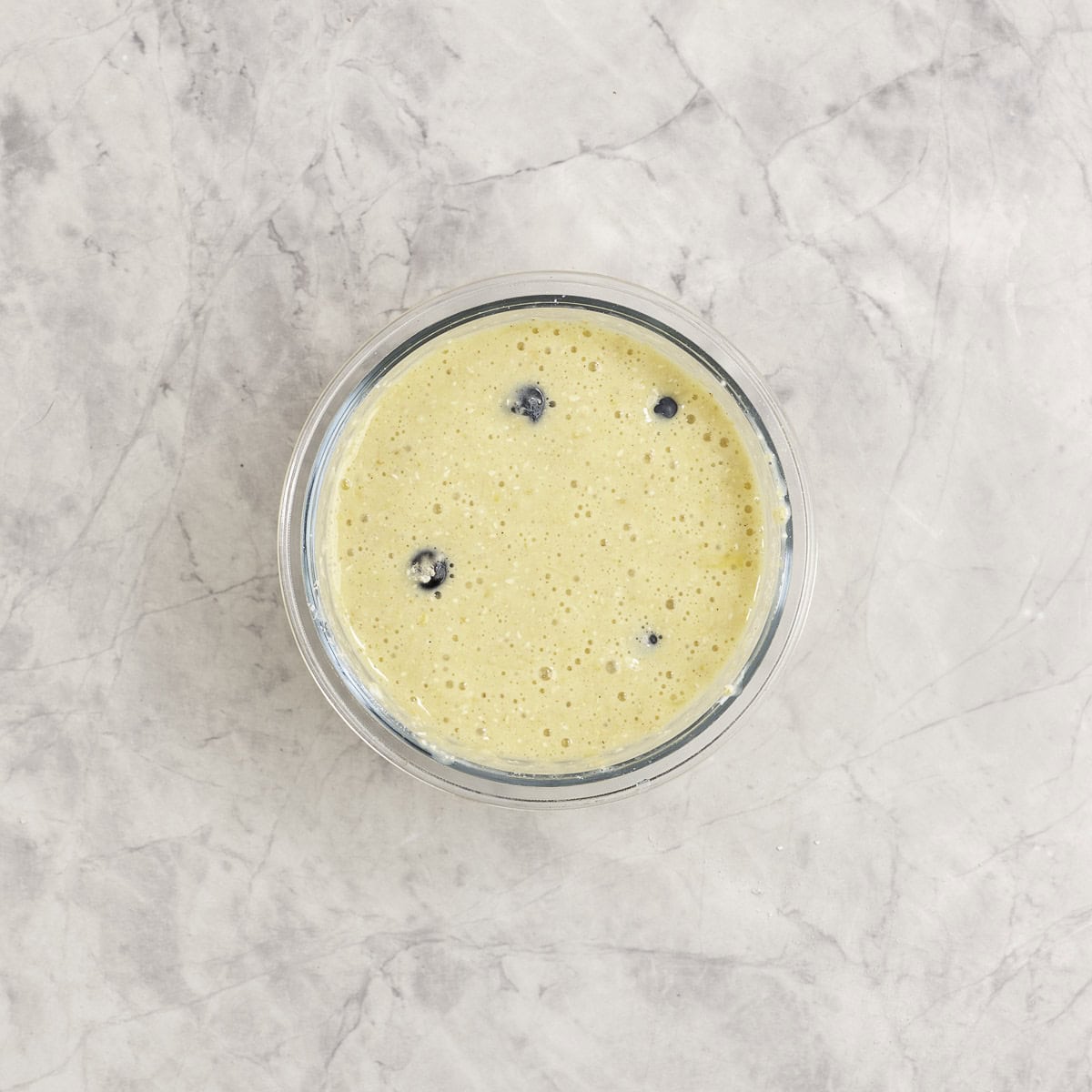 Blueberries added into protein pancake mixture in small glass ramekin.