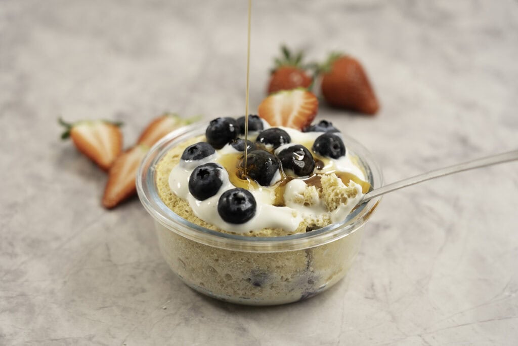 Cooked pancake in a small glass ramekin topped with yogurt, blueberries and maple syrup.