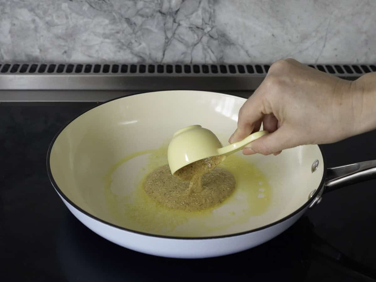 A yellow mixing cup containing pancake mix being poured into a greased pancake pan. 