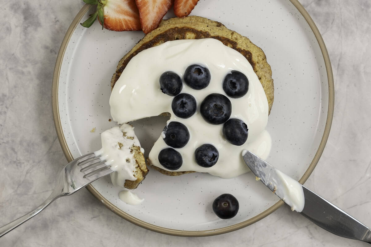 Two stacked pancakes with topped with yogurt, blueberries and strawberries.