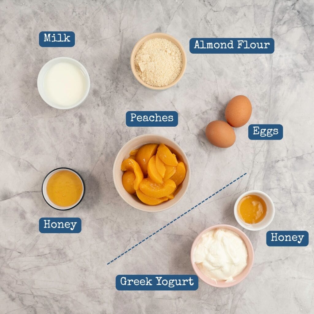 The ingredients to make peach clafoutis laid out on a bench top with text overlay.
