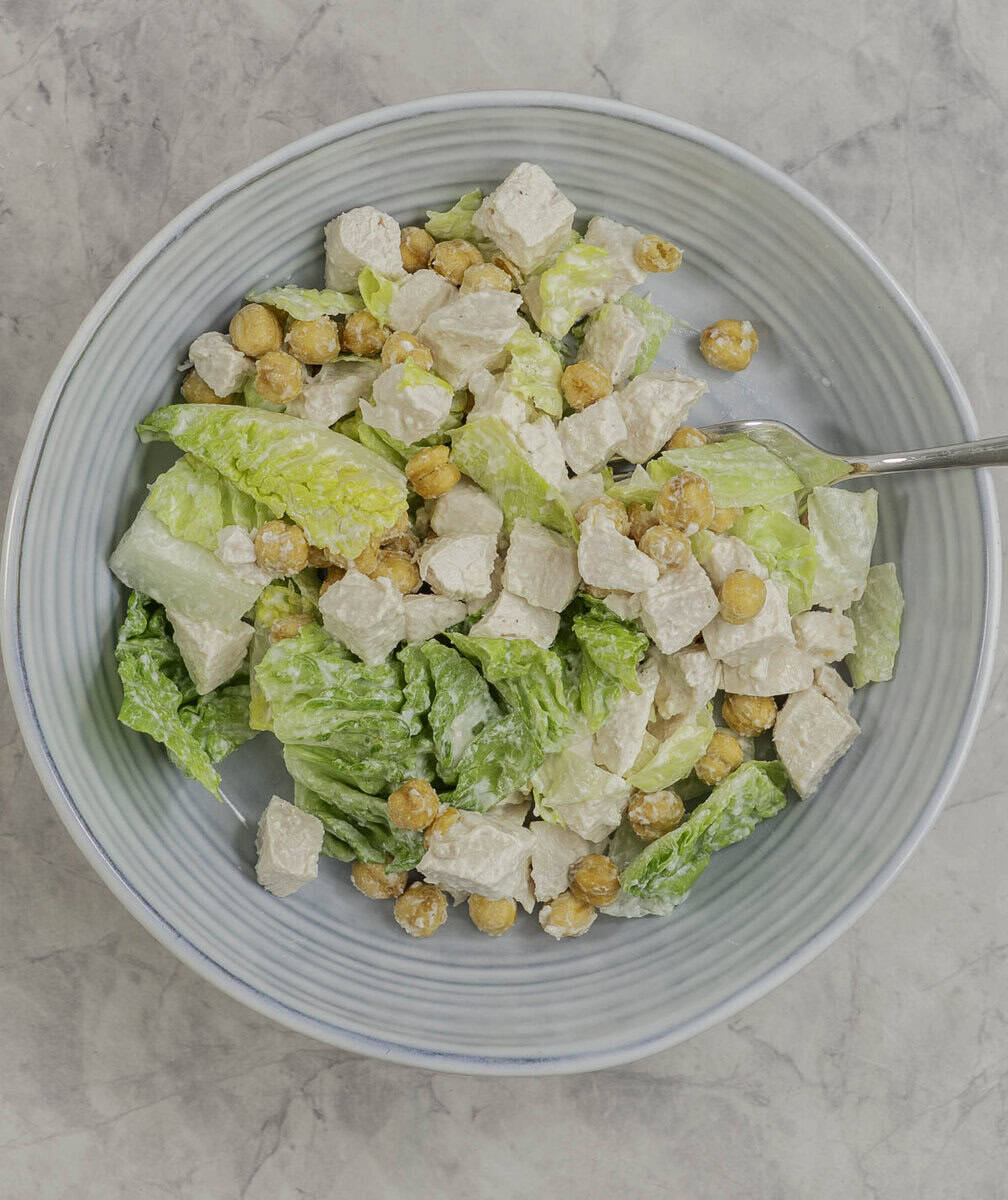 A top down view of chicken Cesar salad with chickpeas in a blue salad bowl with a fork.