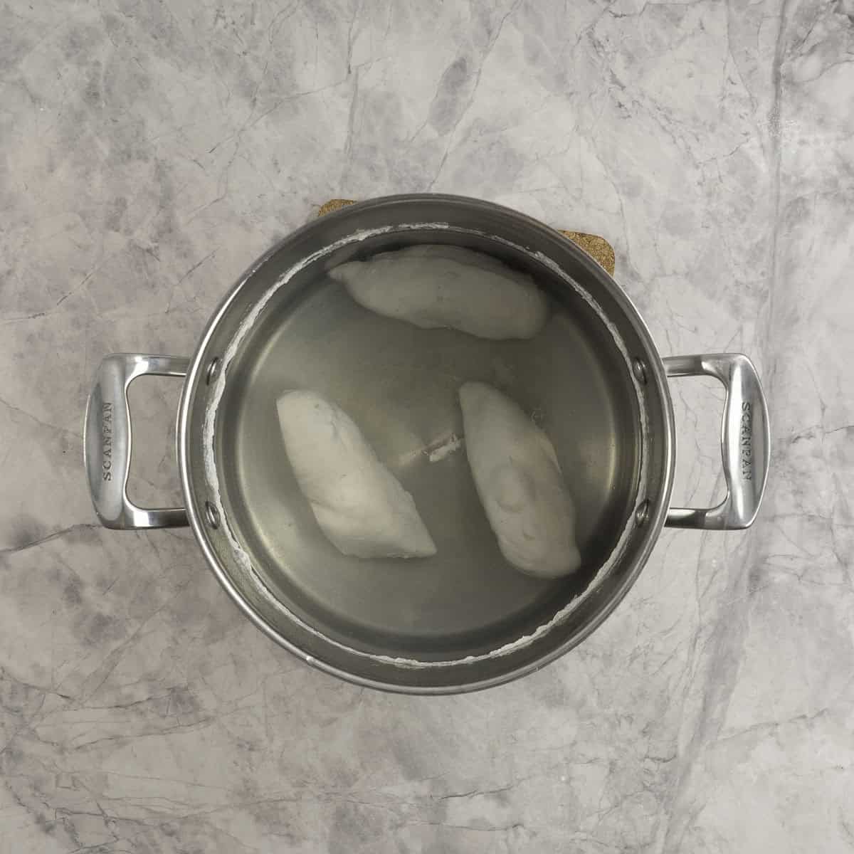 Three poached chicken breasts in a large pot of water. 