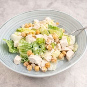 Chicken caesar salad with crispy chicken peas in a blue ribbed salad bowl.
