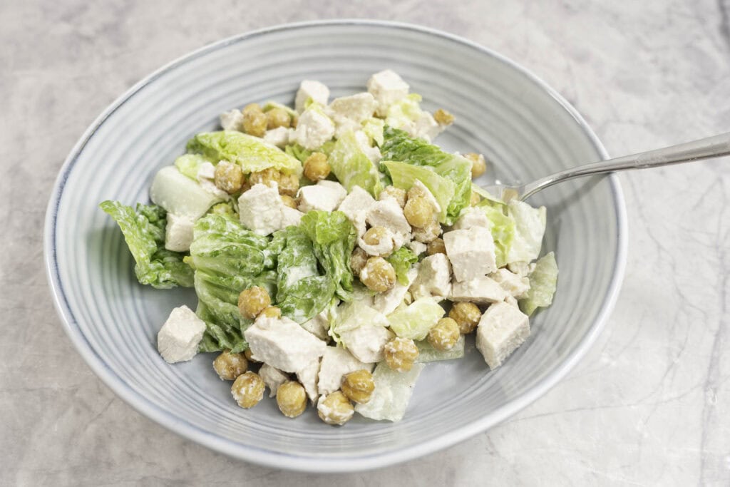 Chicken caesar salad with crispy chicken peas in a blue ribbed salad bowl. 