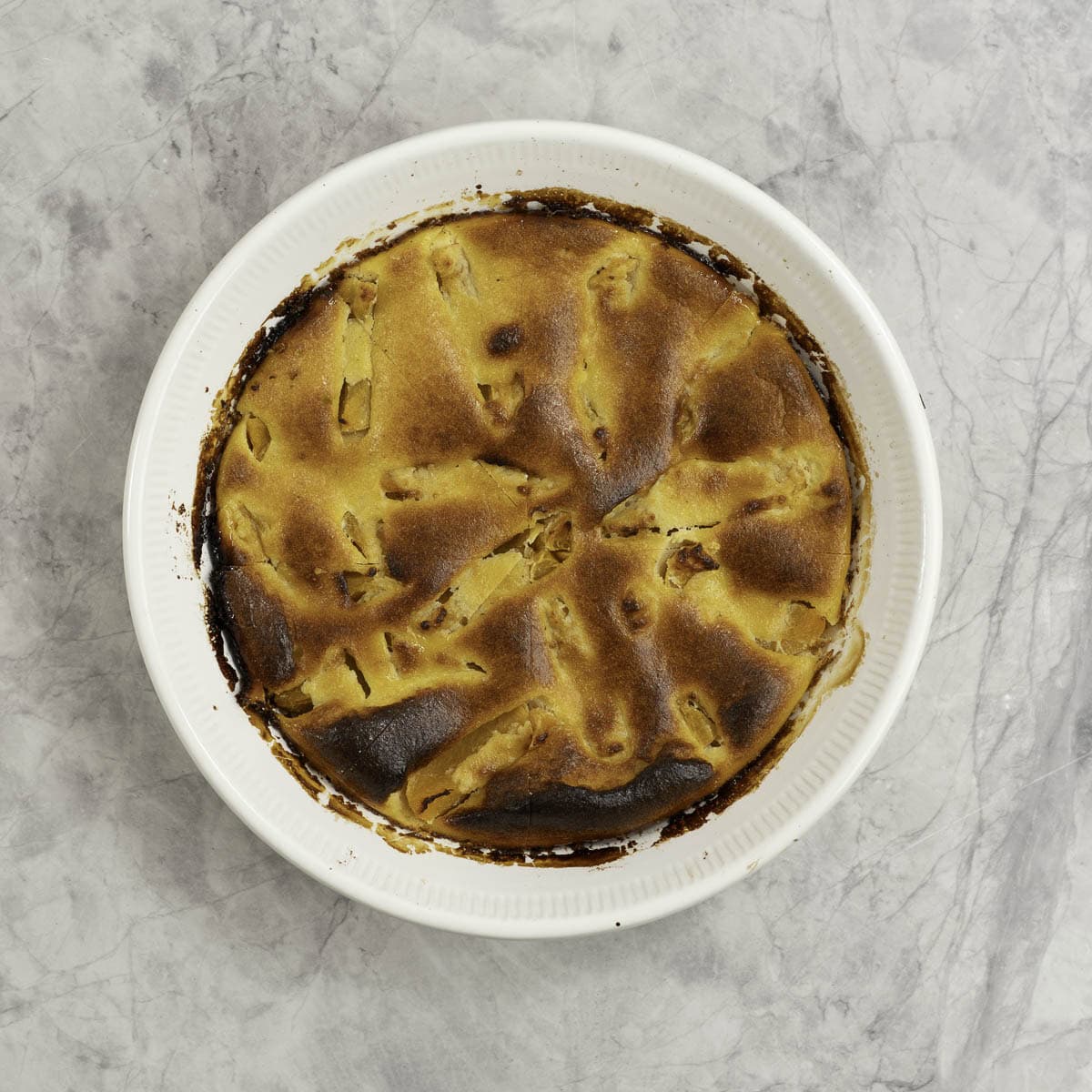 A golden baked pie studded with peach pieces in a white pie dish.