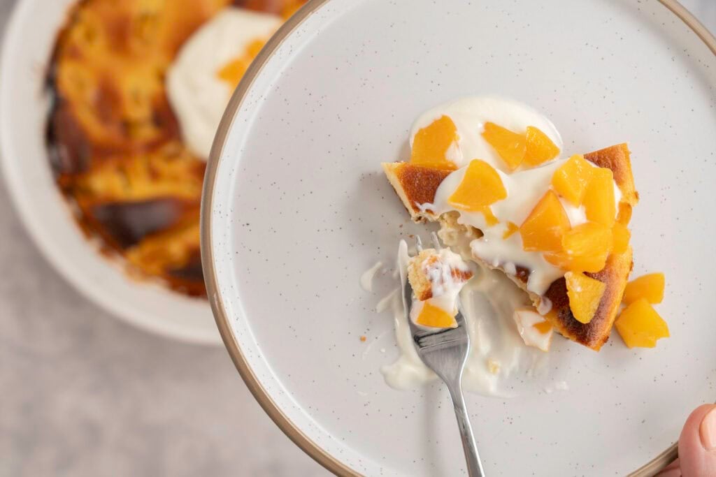A side plate with a slice of clafoutis topped with yogurt and diced peaches.