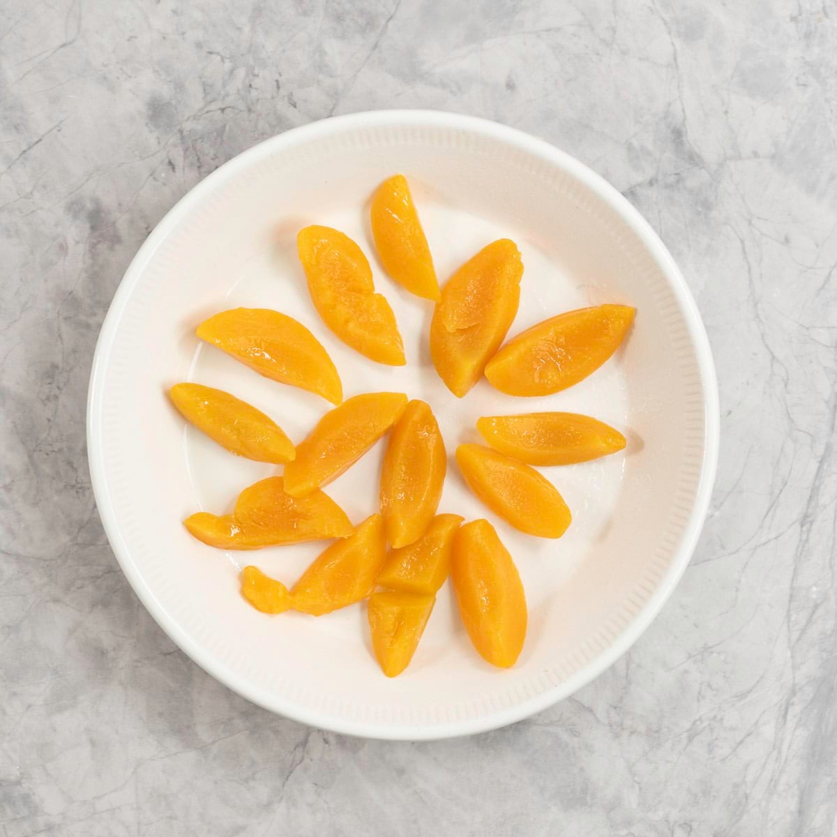 A white ceramic pie dish with slices of peach arranged on the bottom of it.