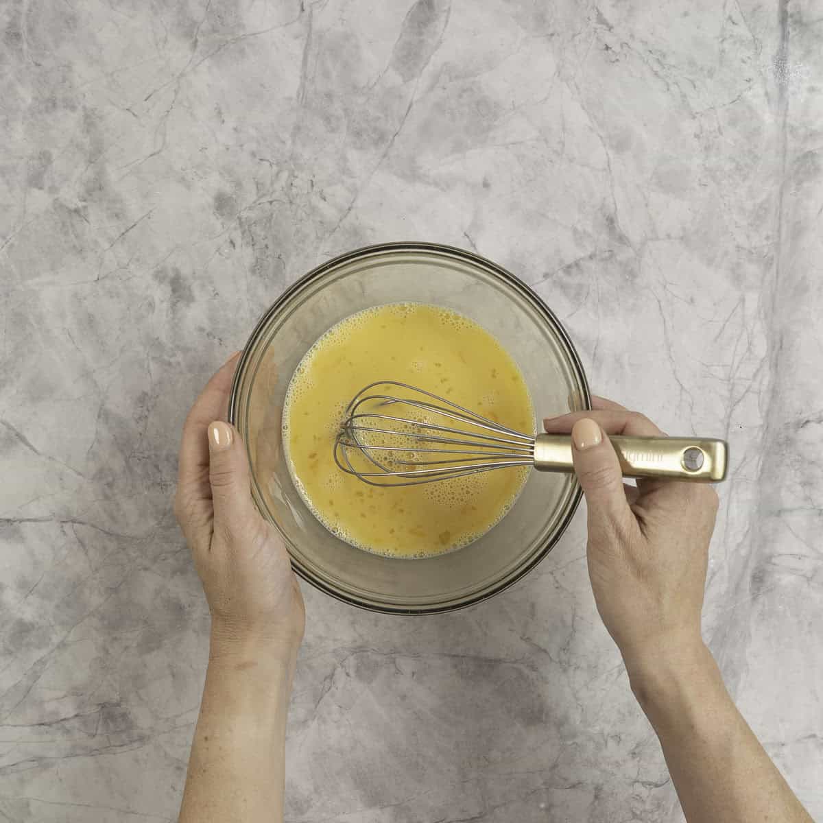 A glass mixing bowl held by one hand with whisked eggs and milk