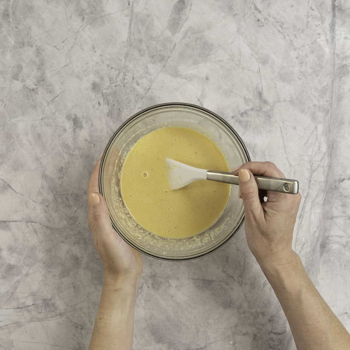 A glass bowl of clafoutis batter being mixed with a spatula