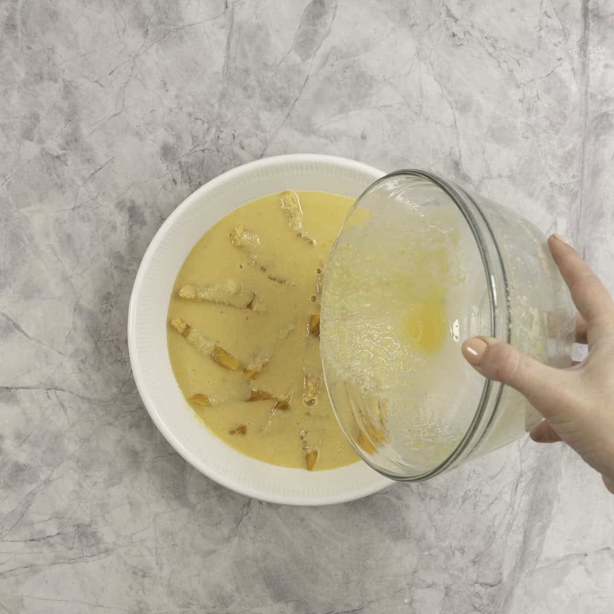 Clafoutis batter being poured into a pie dish lined with peach slices.