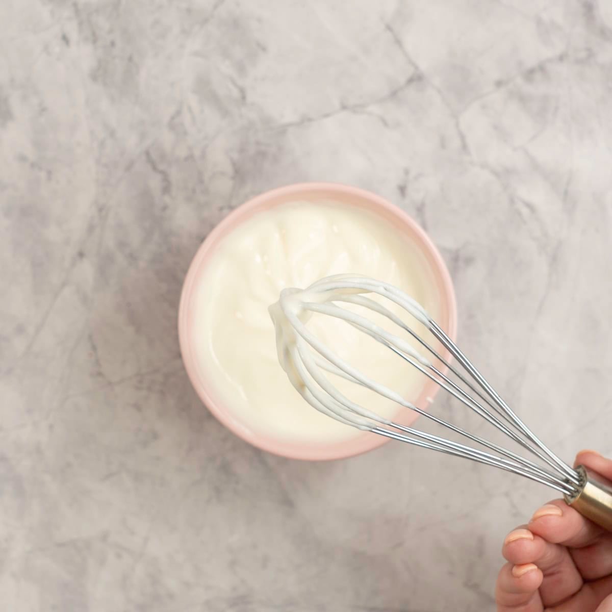 A bowl of smooth honeyed yogurt with a whisk.