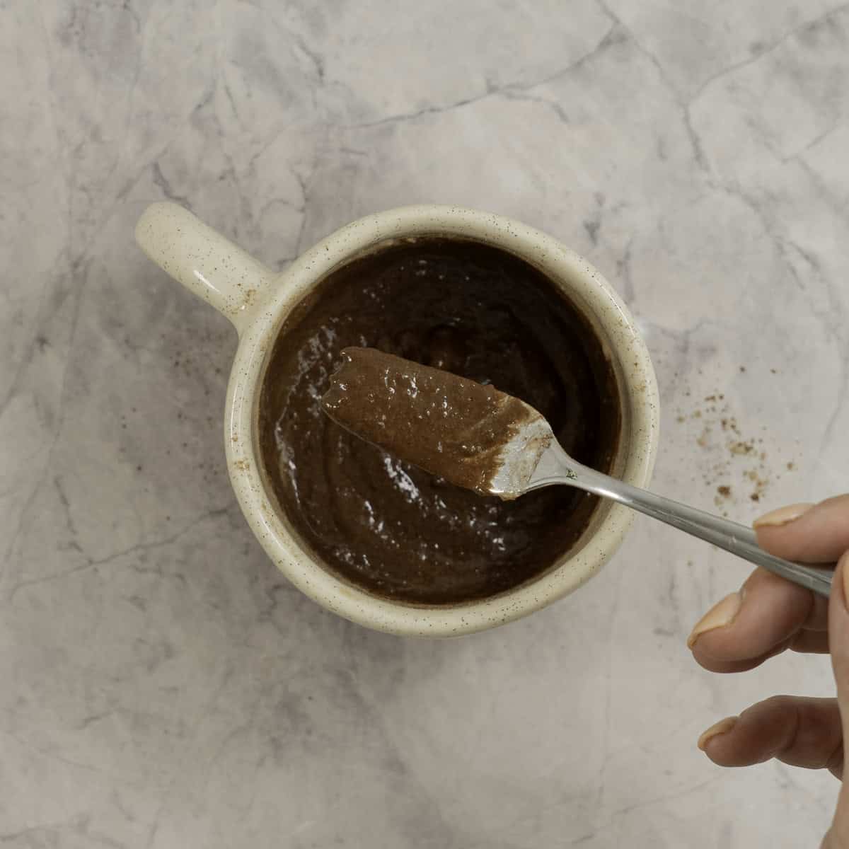 Wet and dry ingredients inside a mug being mixed together with a fork.