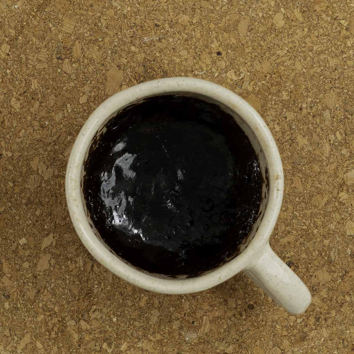 Cooked brownie inside a mug sitting on a cork trivet.