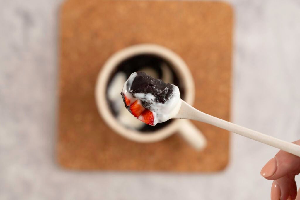 Spoon with brownie, yogurt and strawberries on top held up above mug of brownie.