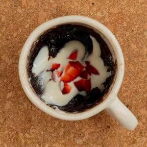 Cooked brownie topped with yogurt and chopped strawberries inside a mug sitting on a cork trivet.