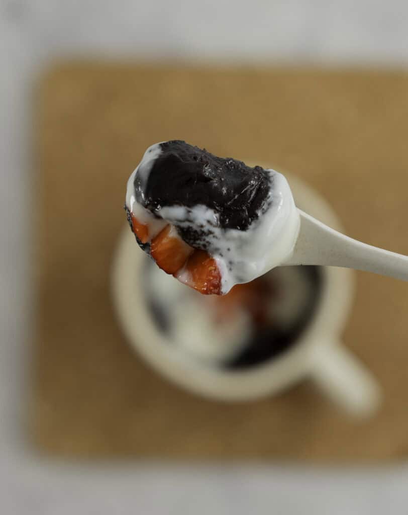Spoon with brownie, yogurt and strawberries on top held up above mug of brownie.