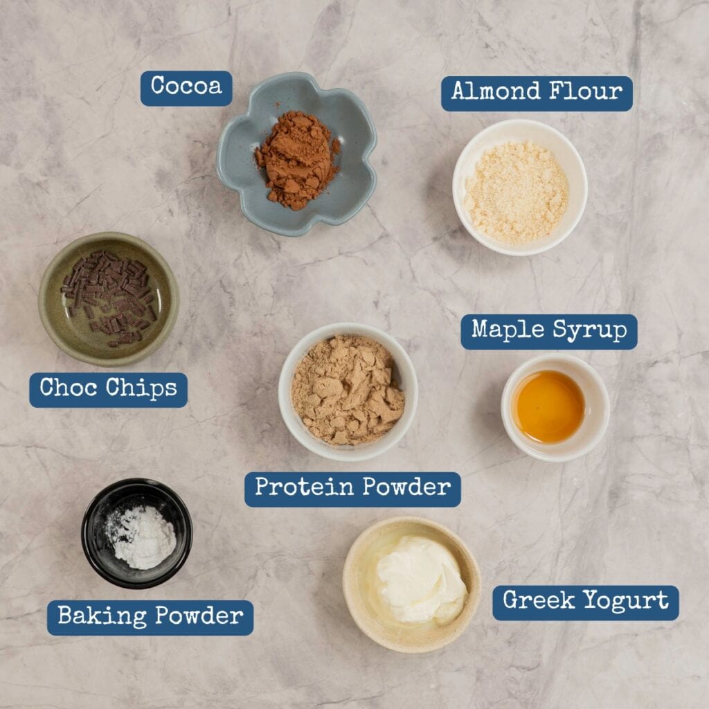 Ingredients for protein mug brownie on benchtop with text overlay.