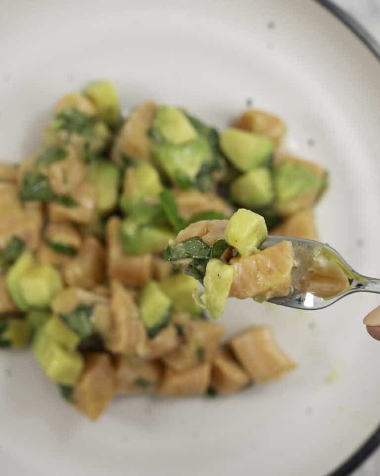 A forkful of salmon tartare above a plate of diced avocado, salmon and shredded mint leaves.