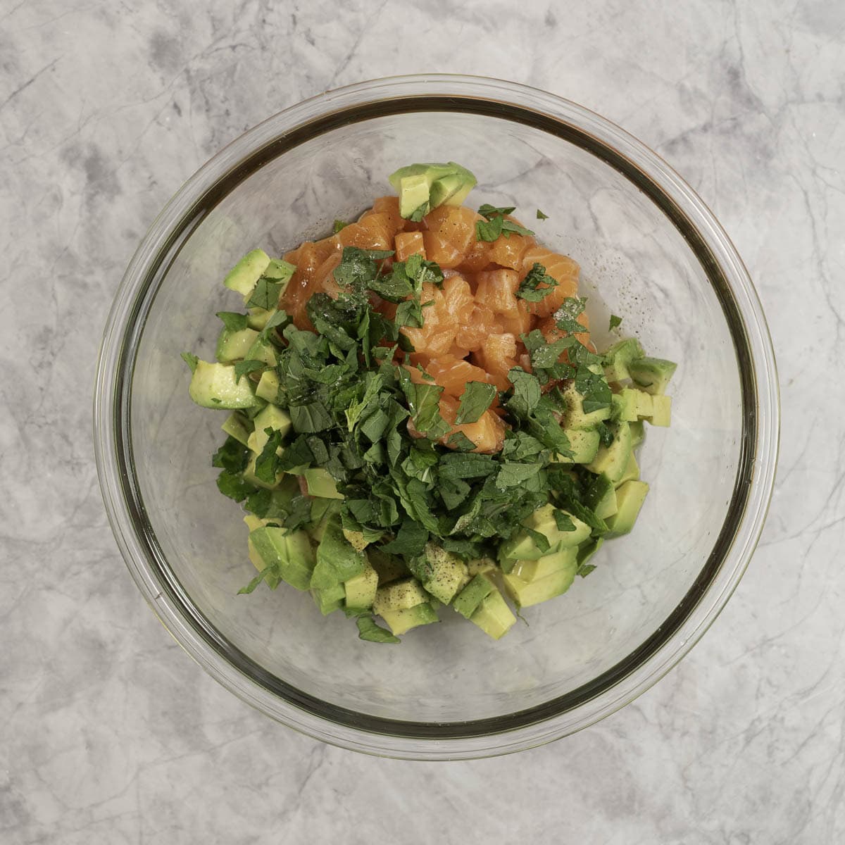 Diced salmon, avocado and mint leaves in a large glass minxing bowl. 