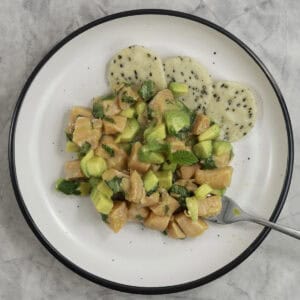 Diced salmon, avocado and mint leaves on a white plate with crisp sesame crackers.